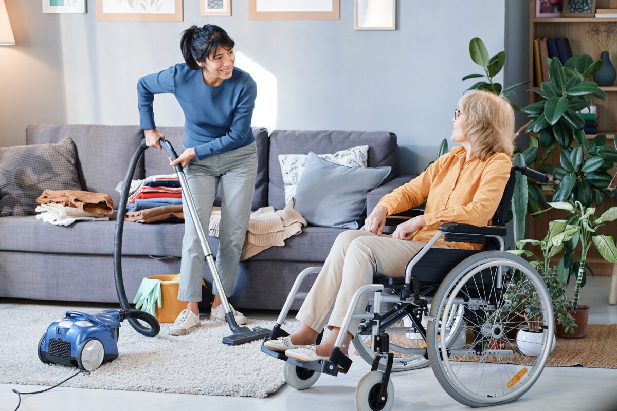 A person in a wheelchair or with a walking aid watching or interacting with a cleaner in a home setting